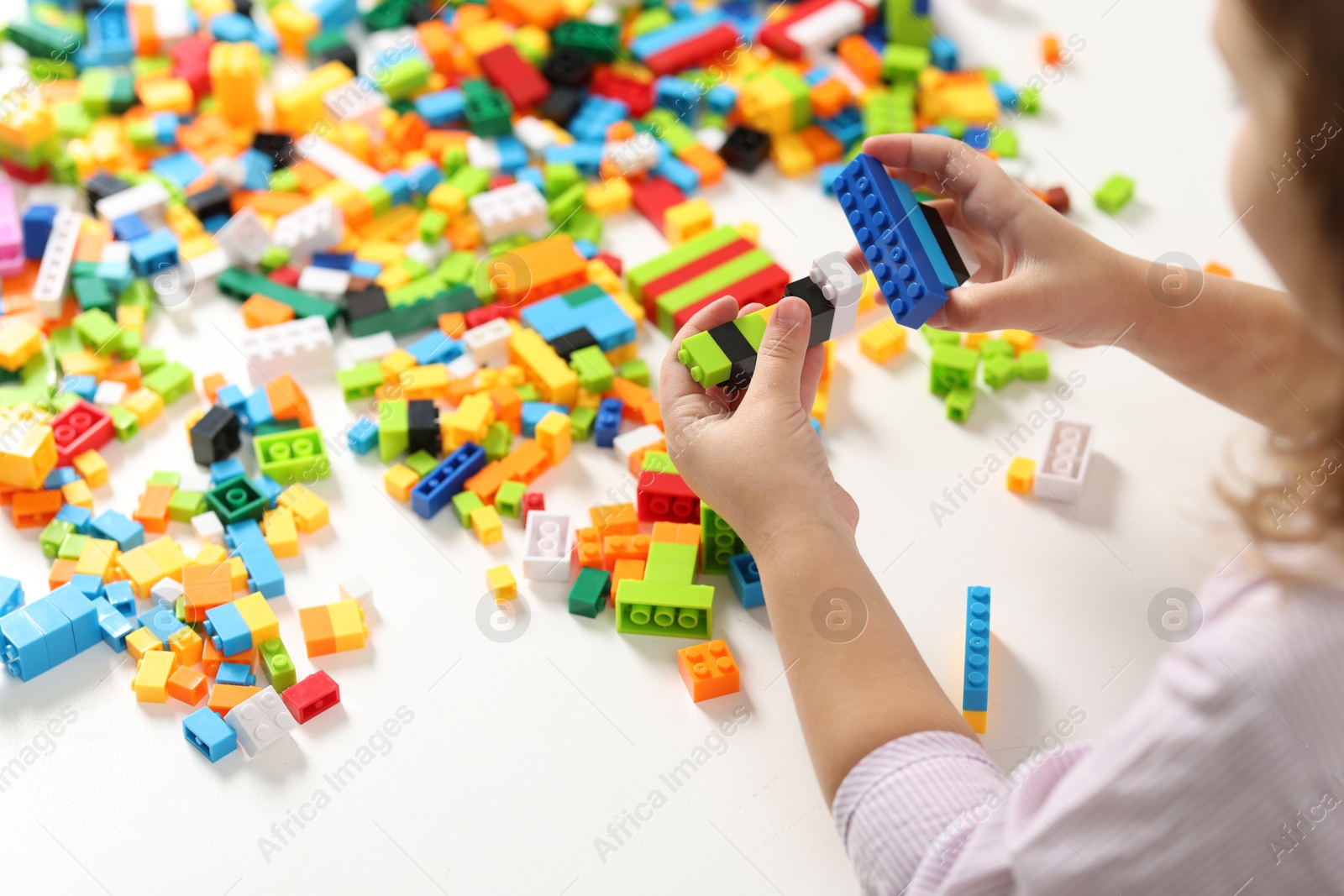 Photo of Girl playing with building blocks at white table indoors, closeup