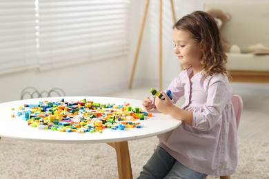 Photo of Cute girl playing with building blocks at white table indoors