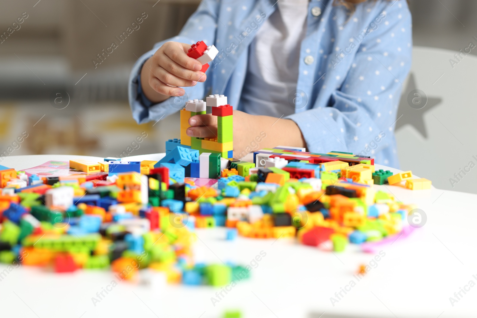 Photo of Girl playing with building blocks at white table indoors, closeup