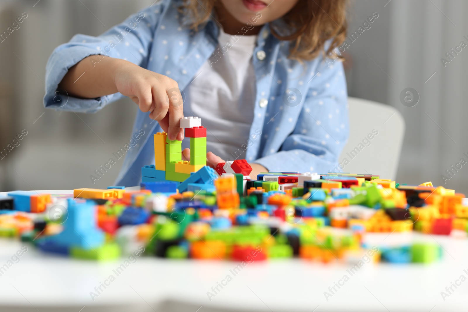 Photo of Girl playing with building blocks at white table indoors, closeup