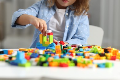 Photo of Girl playing with building blocks at white table indoors, closeup