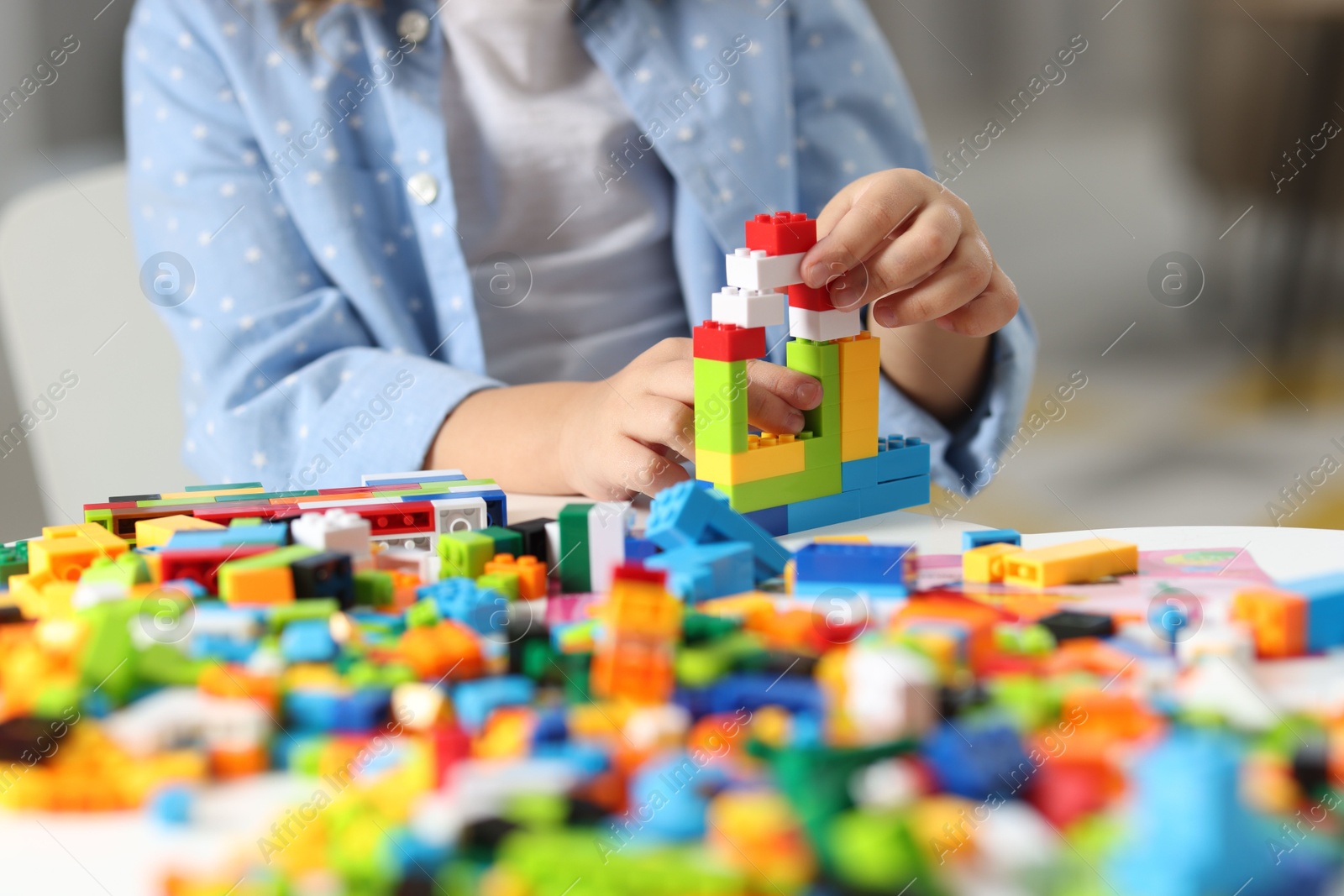 Photo of Girl playing with building blocks at white table indoors, closeup