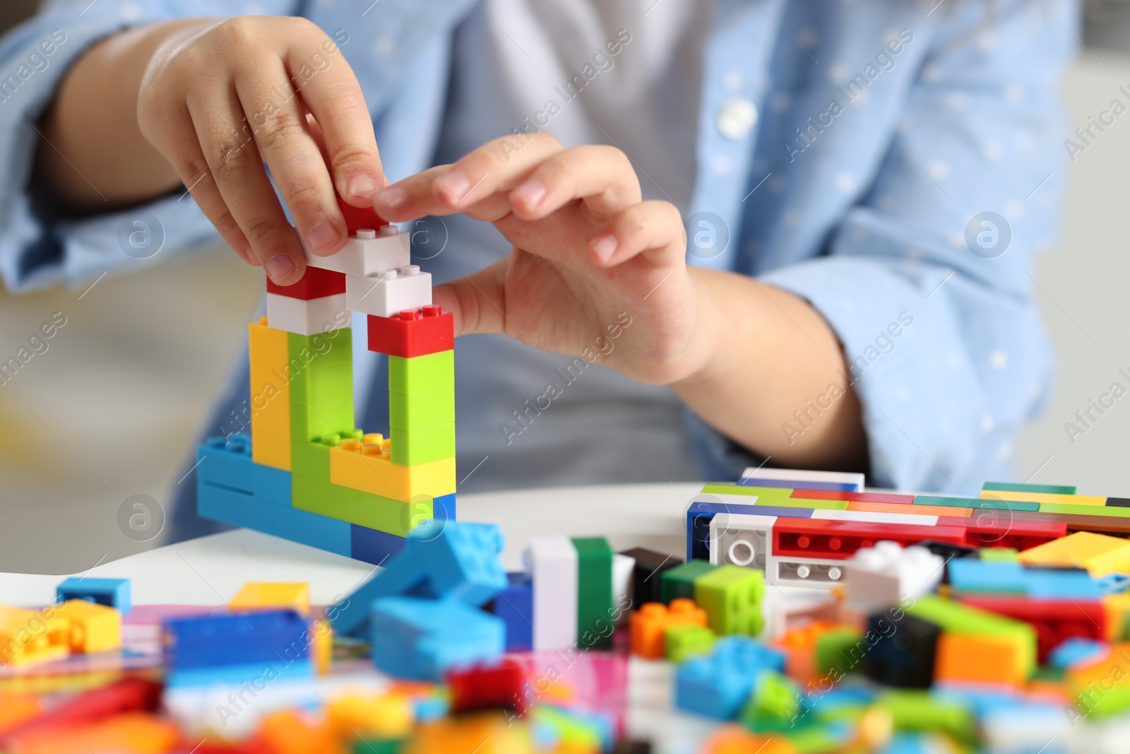 Photo of Girl playing with building blocks at white table indoors, closeup