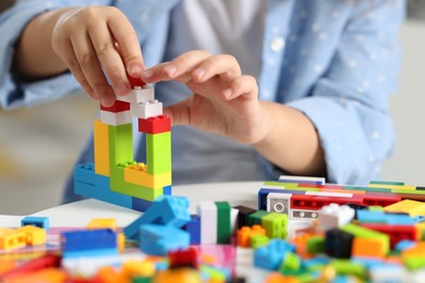 Photo of Girl playing with building blocks at white table indoors, closeup