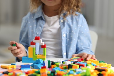 Photo of Girl playing with building blocks at white table indoors, closeup