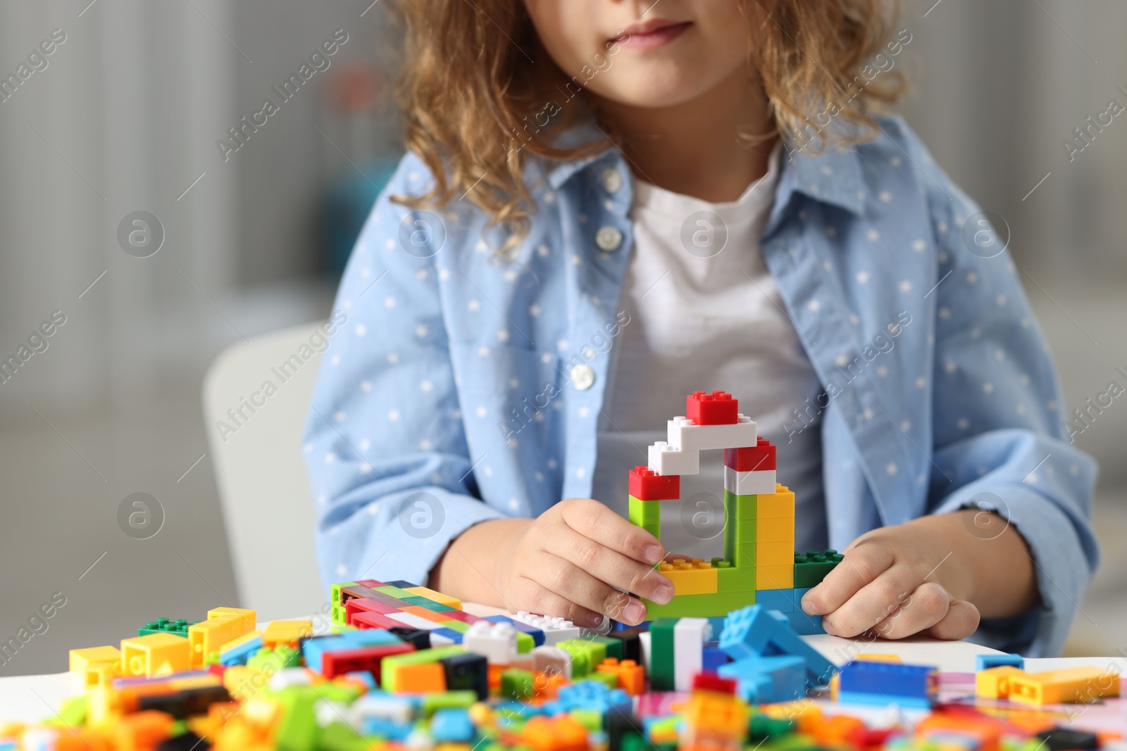 Photo of Girl playing with building blocks at white table indoors, closeup