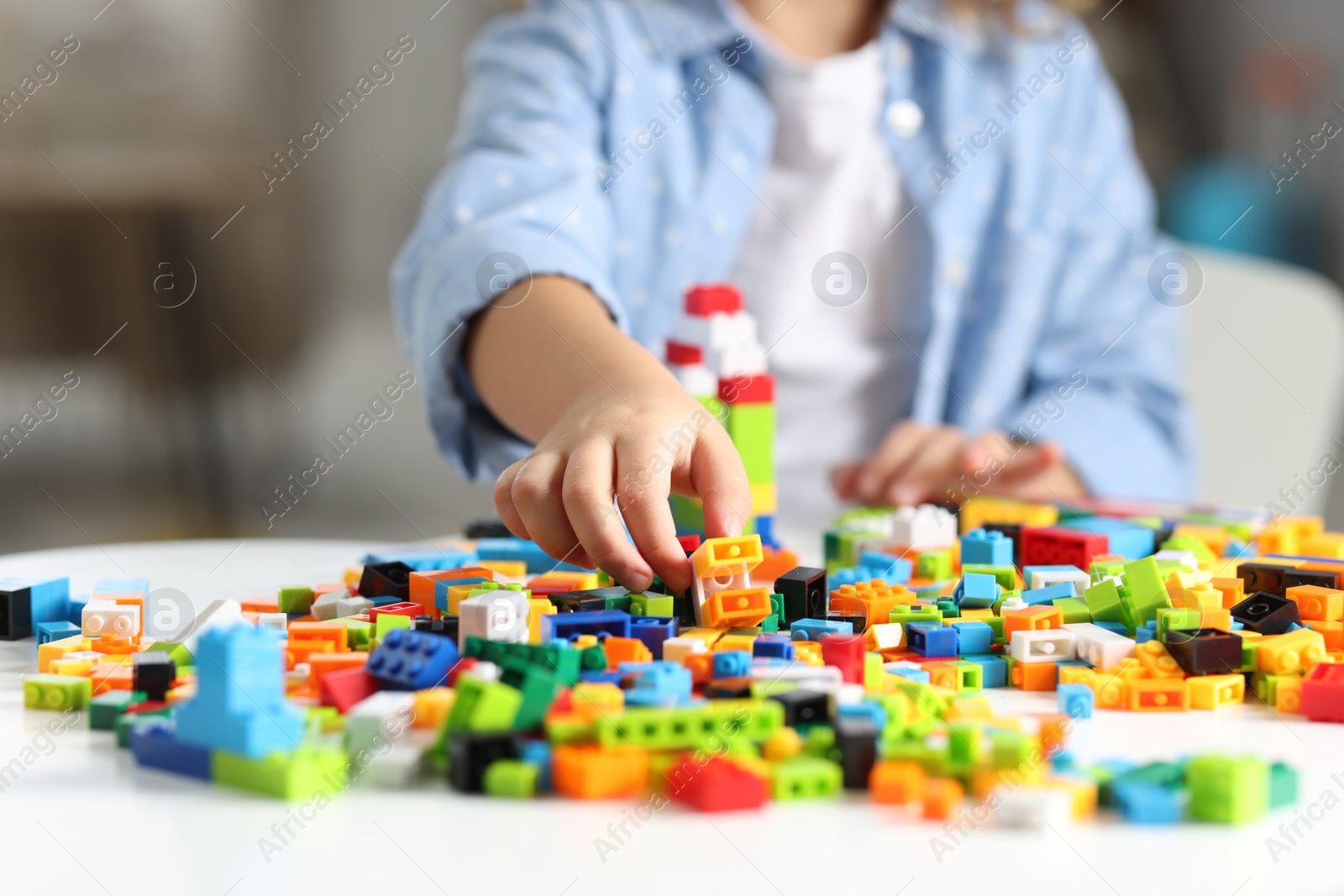 Photo of Girl playing with building blocks at white table indoors, closeup