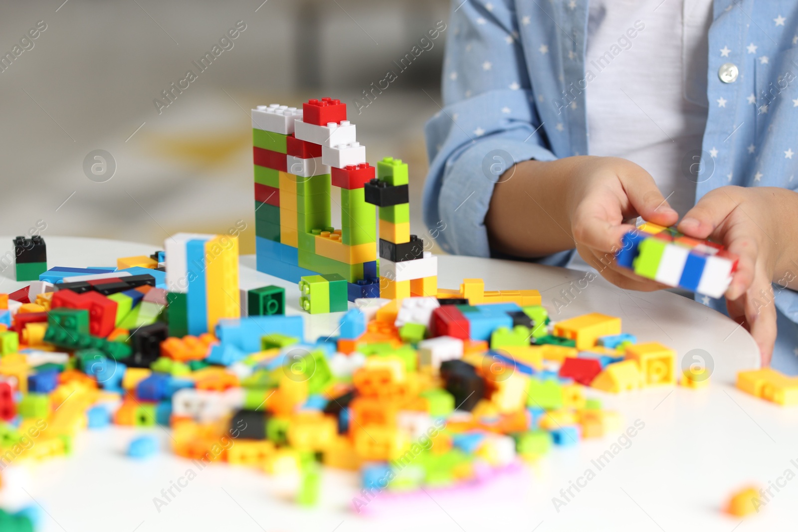 Photo of Girl playing with building blocks at white table indoors, closeup