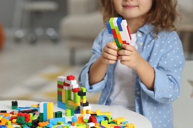 Photo of Girl playing with building blocks at white table indoors, closeup