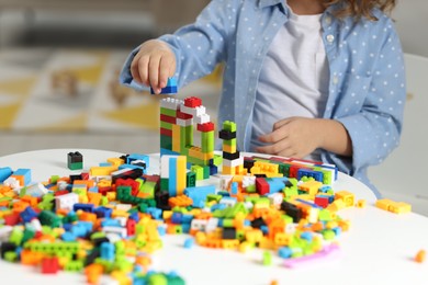 Photo of Girl playing with building blocks at white table indoors, closeup