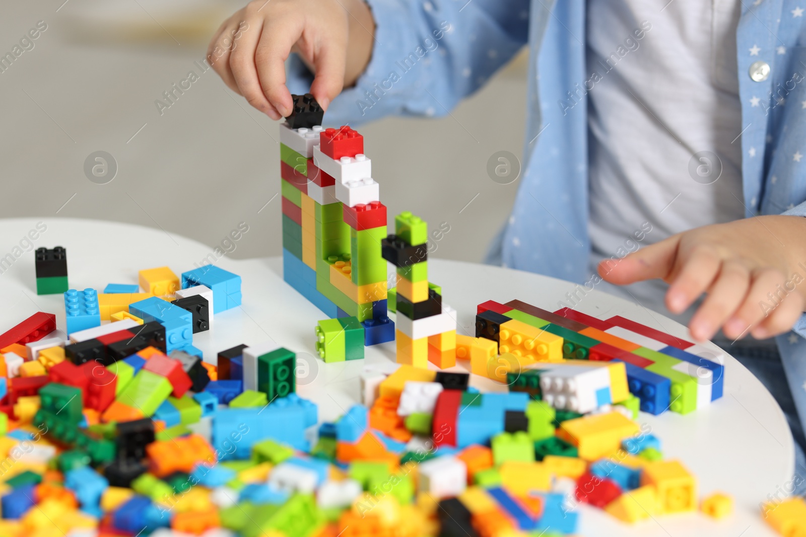 Photo of Girl playing with building blocks at white table indoors, closeup