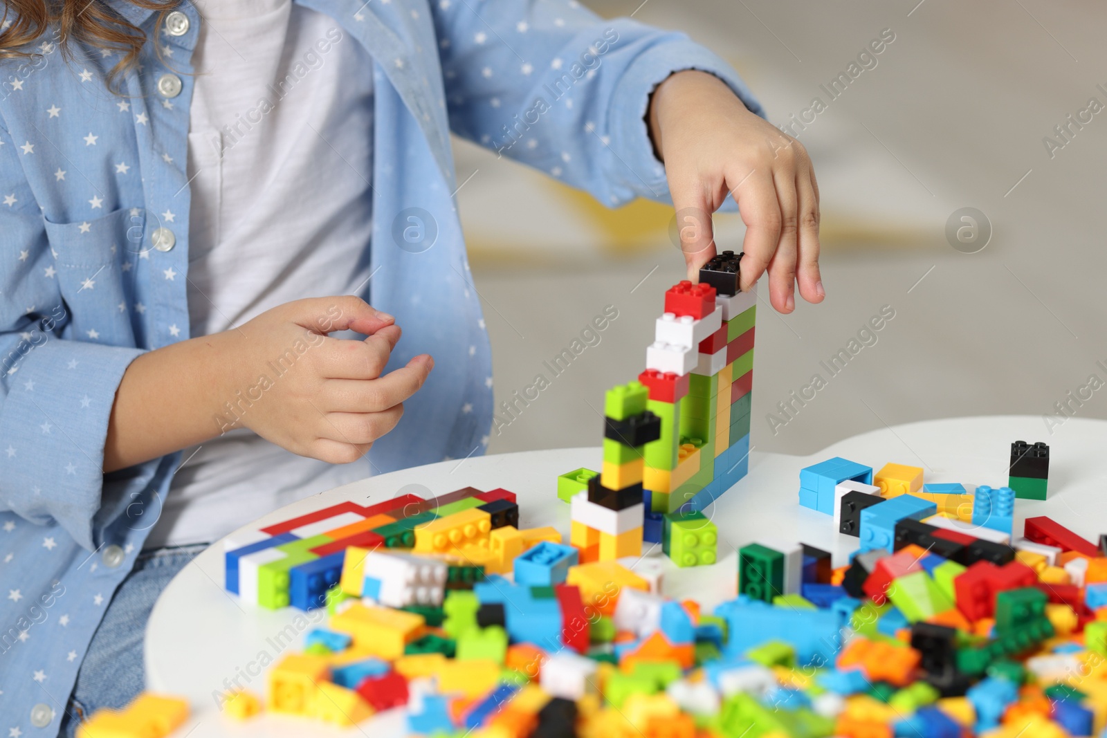 Photo of Girl playing with building blocks at white table indoors, closeup