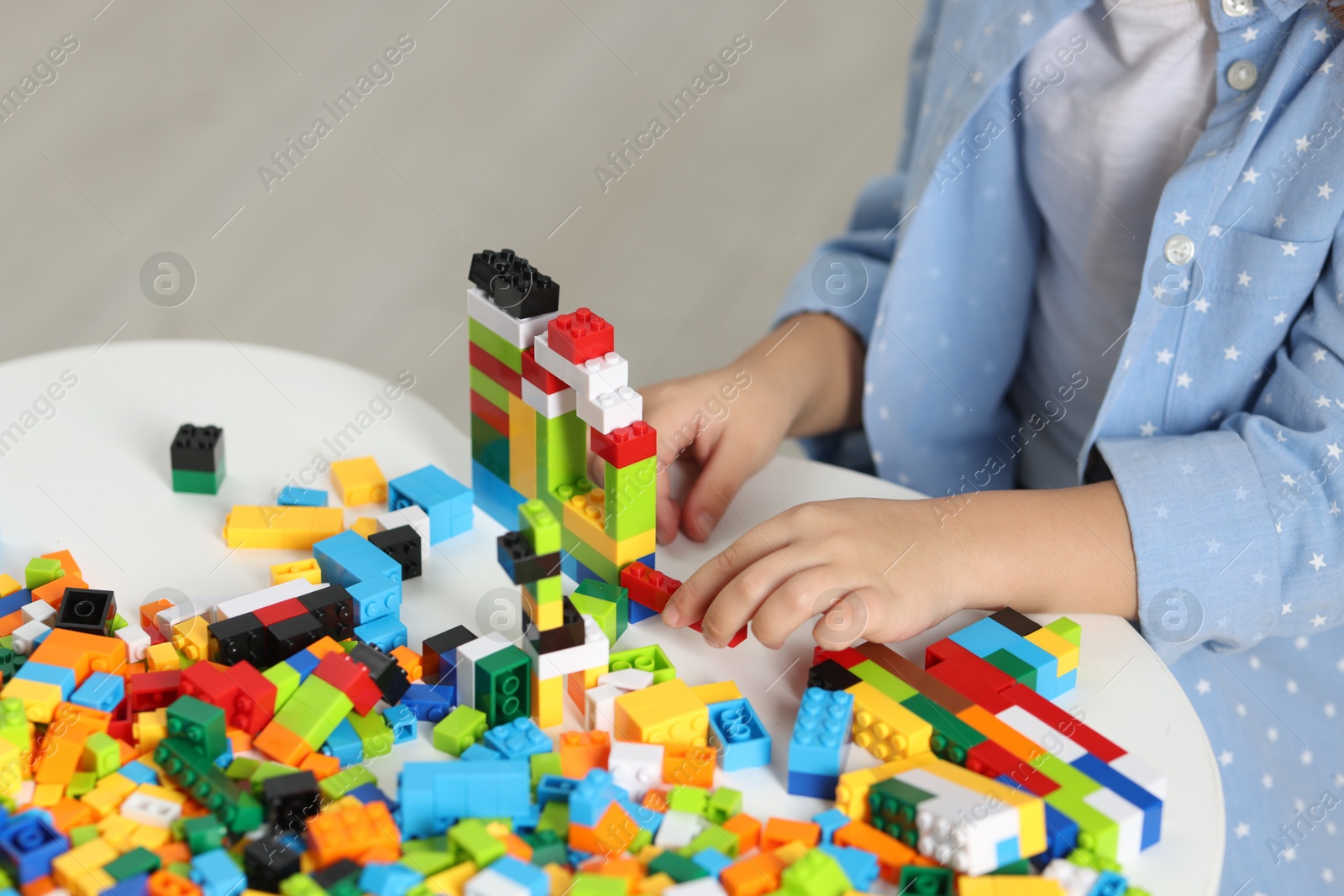 Photo of Girl playing with building blocks at white table indoors, closeup