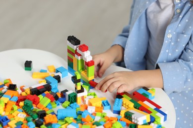 Photo of Girl playing with building blocks at white table indoors, closeup