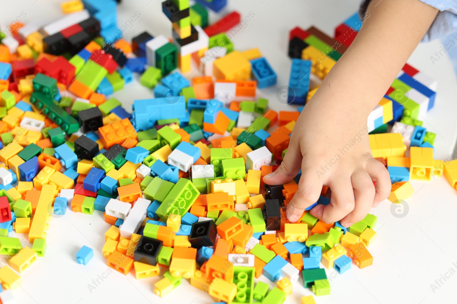 Photo of Girl playing with building blocks at white table indoors, closeup