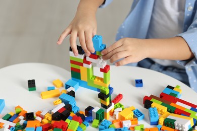 Photo of Girl playing with building blocks at white table indoors, closeup