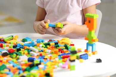 Photo of Girl playing with building blocks at white table indoors, closeup