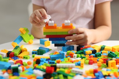 Photo of Girl playing with building blocks at white table indoors, closeup