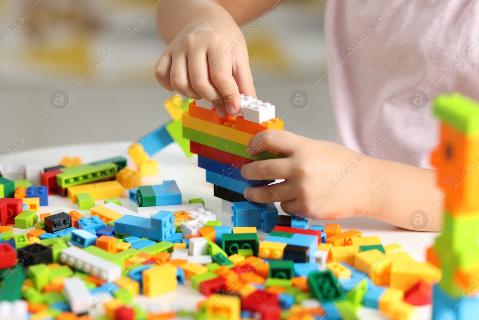 Photo of Girl playing with building blocks at white table indoors, closeup