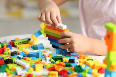 Photo of Girl playing with building blocks at white table indoors, closeup