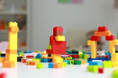 Photo of Construction toy. Figures made with building bricks and colorful blocks on white table indoors, closeup