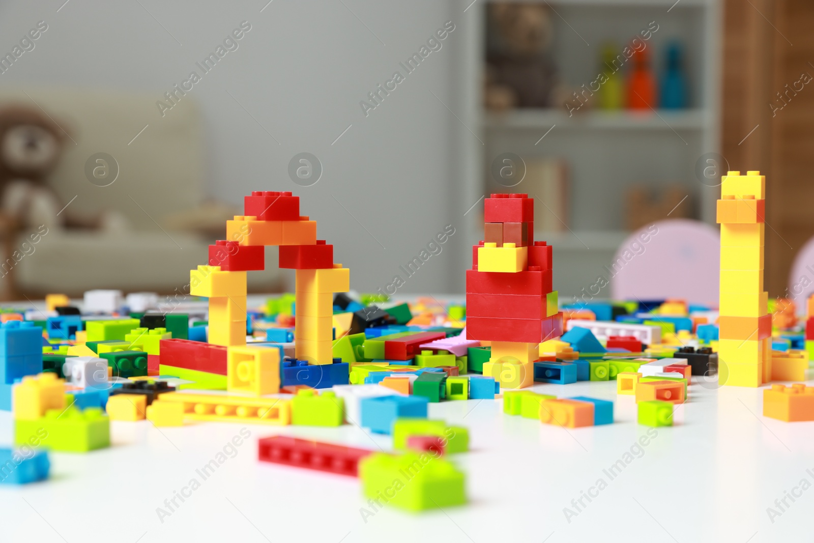 Photo of Construction toy. Figures made with building bricks and colorful blocks on white table indoors, closeup