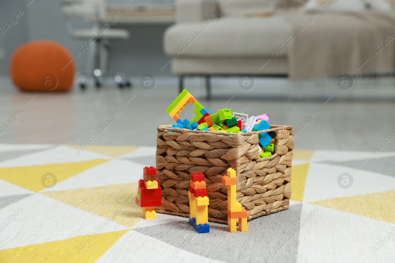 Photo of Construction toy. Figures made with building bricks and wicker basket of blocks on floor indoors, space for text