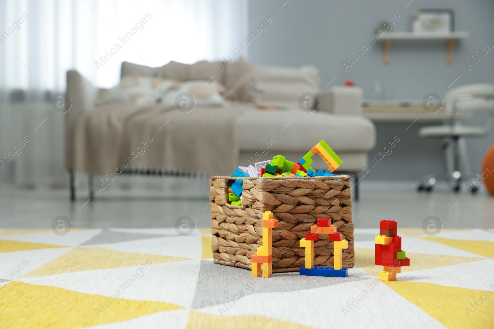 Photo of Construction toy. Figures made with building bricks and wicker basket of blocks on floor indoors, space for text