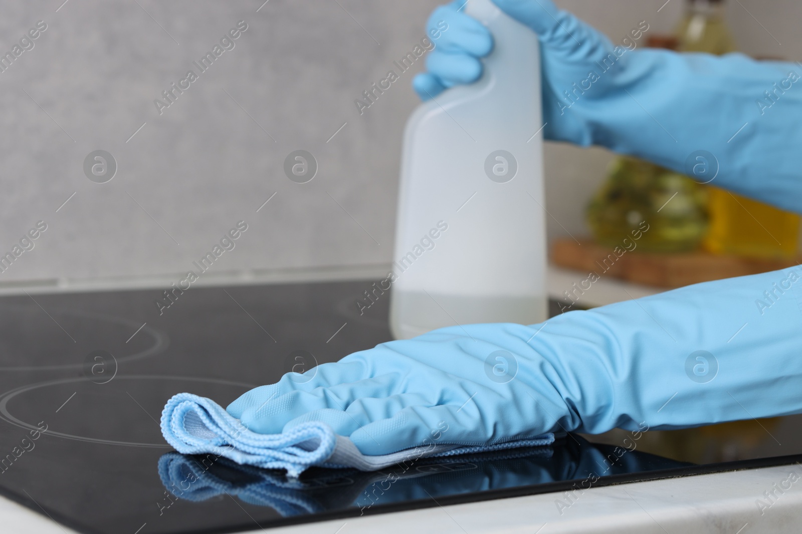 Photo of Woman using cleaning product while wiping induction cooktop with rag in kitchen, closeup