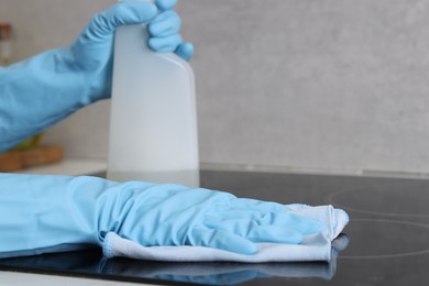 Photo of Woman using cleaning product while wiping induction cooktop with rag in kitchen, closeup