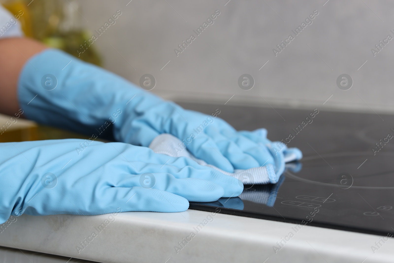 Photo of Woman cleaning induction cooktop with rag in kitchen, closeup. Space for text