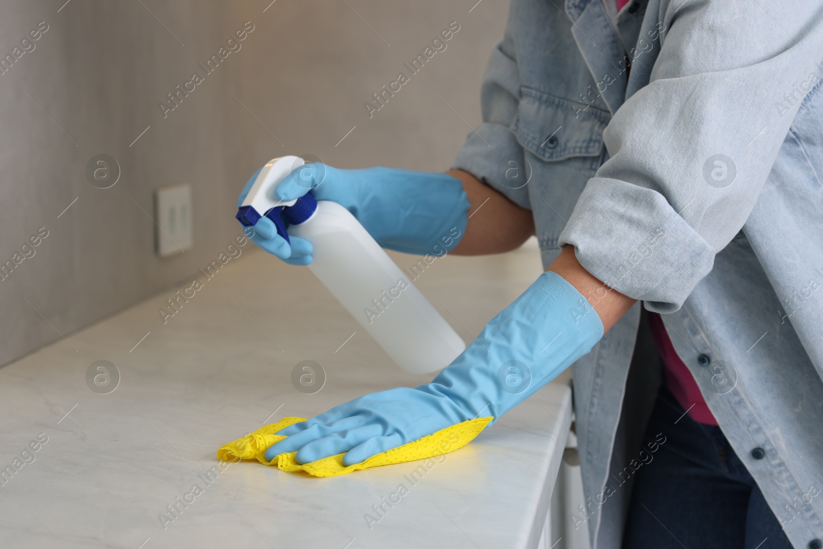 Photo of Woman using cleaning product while wiping countertop with rag indoors, closeup