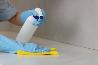 Photo of Woman using cleaning product while wiping countertop with rag indoors, closeup. Space for text