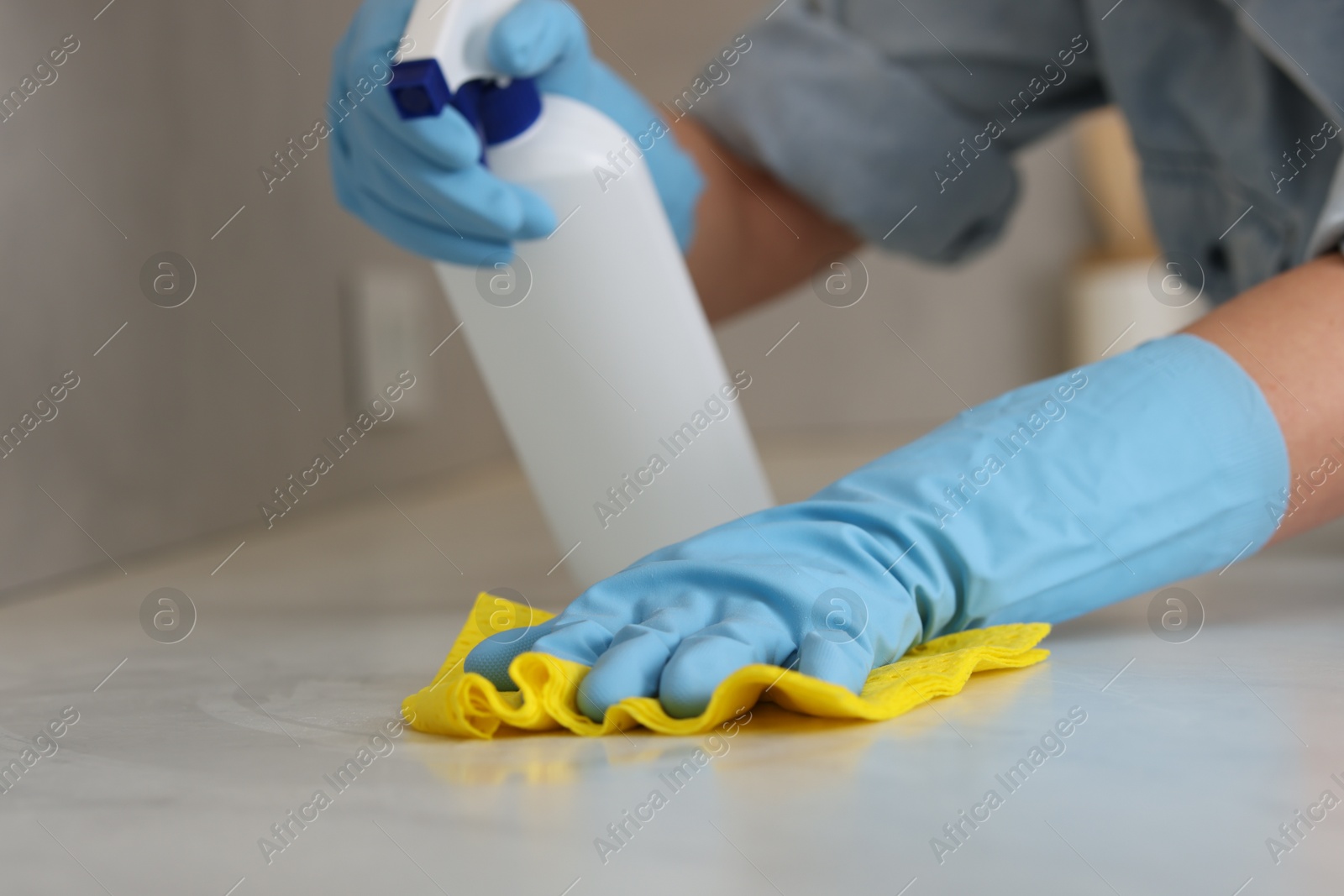 Photo of Woman using cleaning product while wiping countertop with rag indoors, closeup