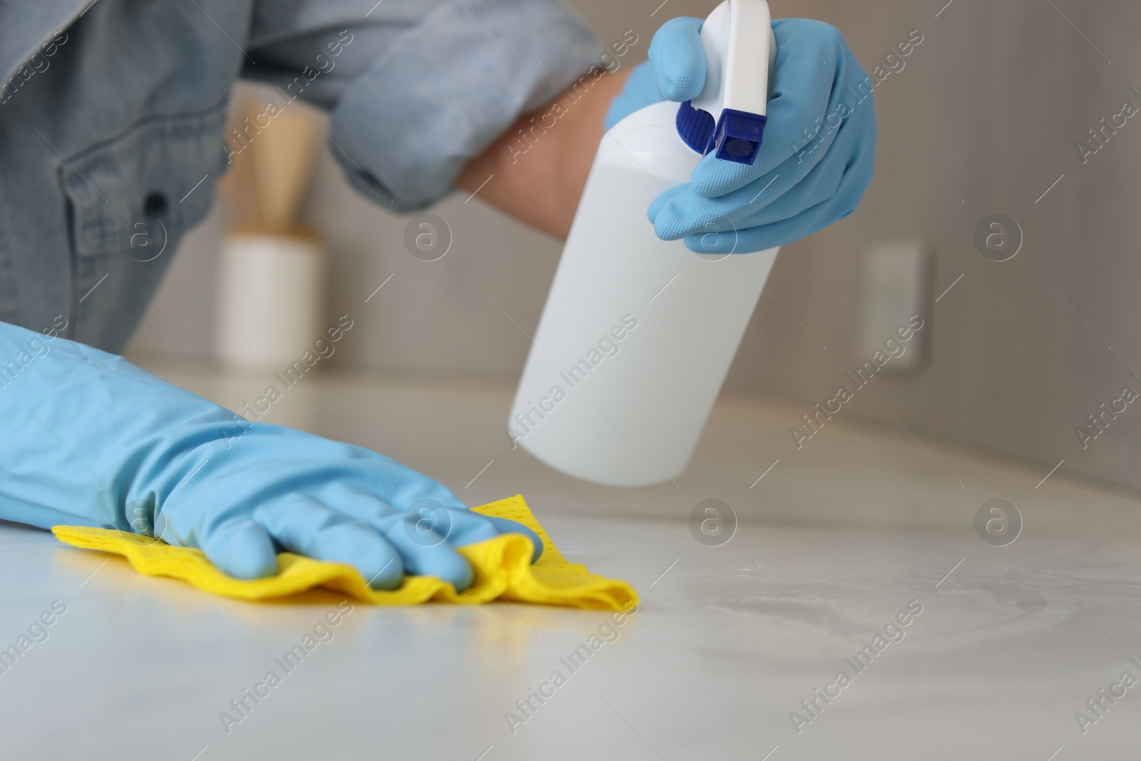 Photo of Woman using cleaning product while wiping countertop with rag indoors, closeup