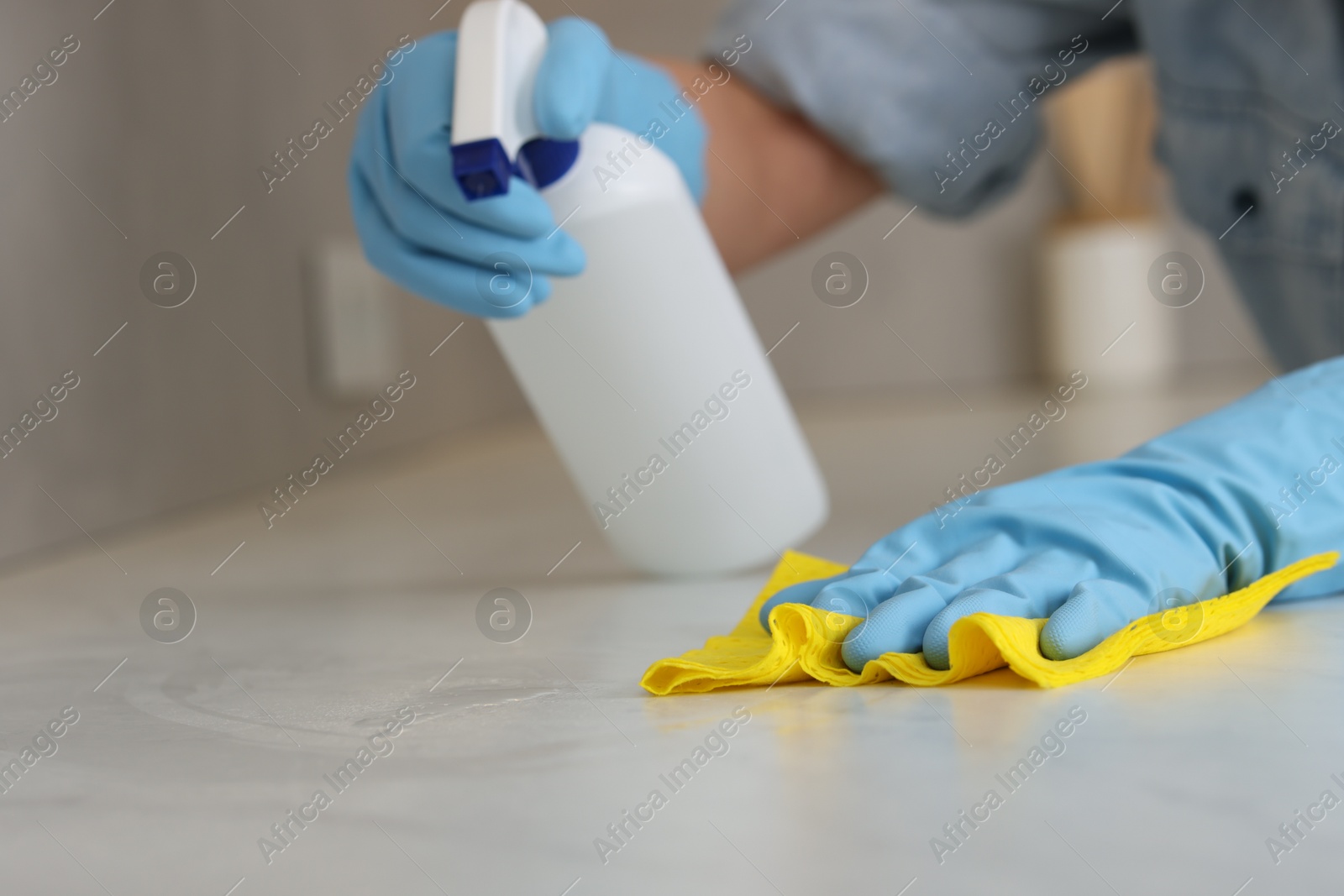 Photo of Woman using cleaning product while wiping countertop with rag indoors, closeup