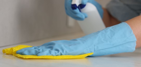 Photo of Woman using cleaning product while wiping countertop with rag indoors, closeup