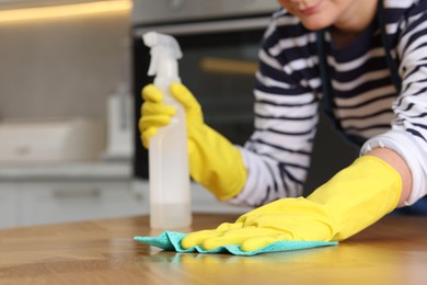 Photo of Woman using cleaning product while wiping wooden table with rag indoors, closeup