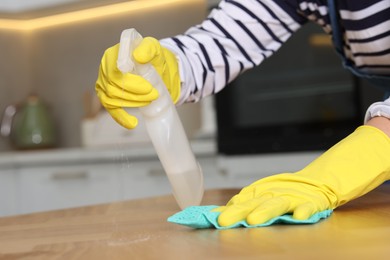 Photo of Woman using cleaning product while wiping wooden table with rag indoors, closeup