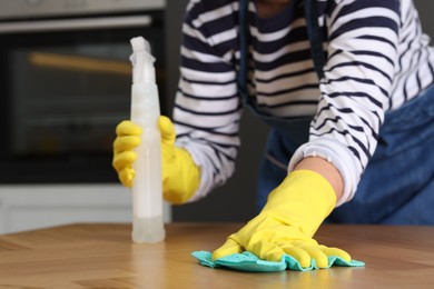 Photo of Woman using cleaning product while wiping wooden table with rag indoors, closeup