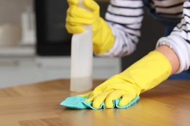 Photo of Woman using cleaning product while wiping wooden table with rag indoors, closeup