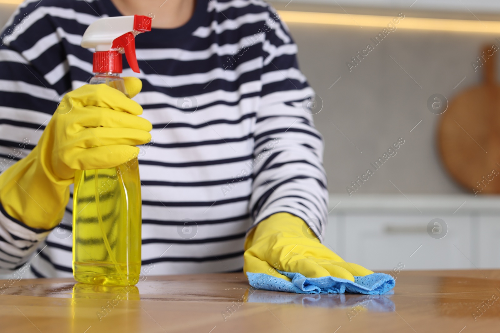 Photo of Woman using cleaning product while wiping wooden table with rag indoors, closeup. Space for text