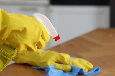 Photo of Woman using cleaning product while wiping wooden table with rag indoors, closeup. Space for text