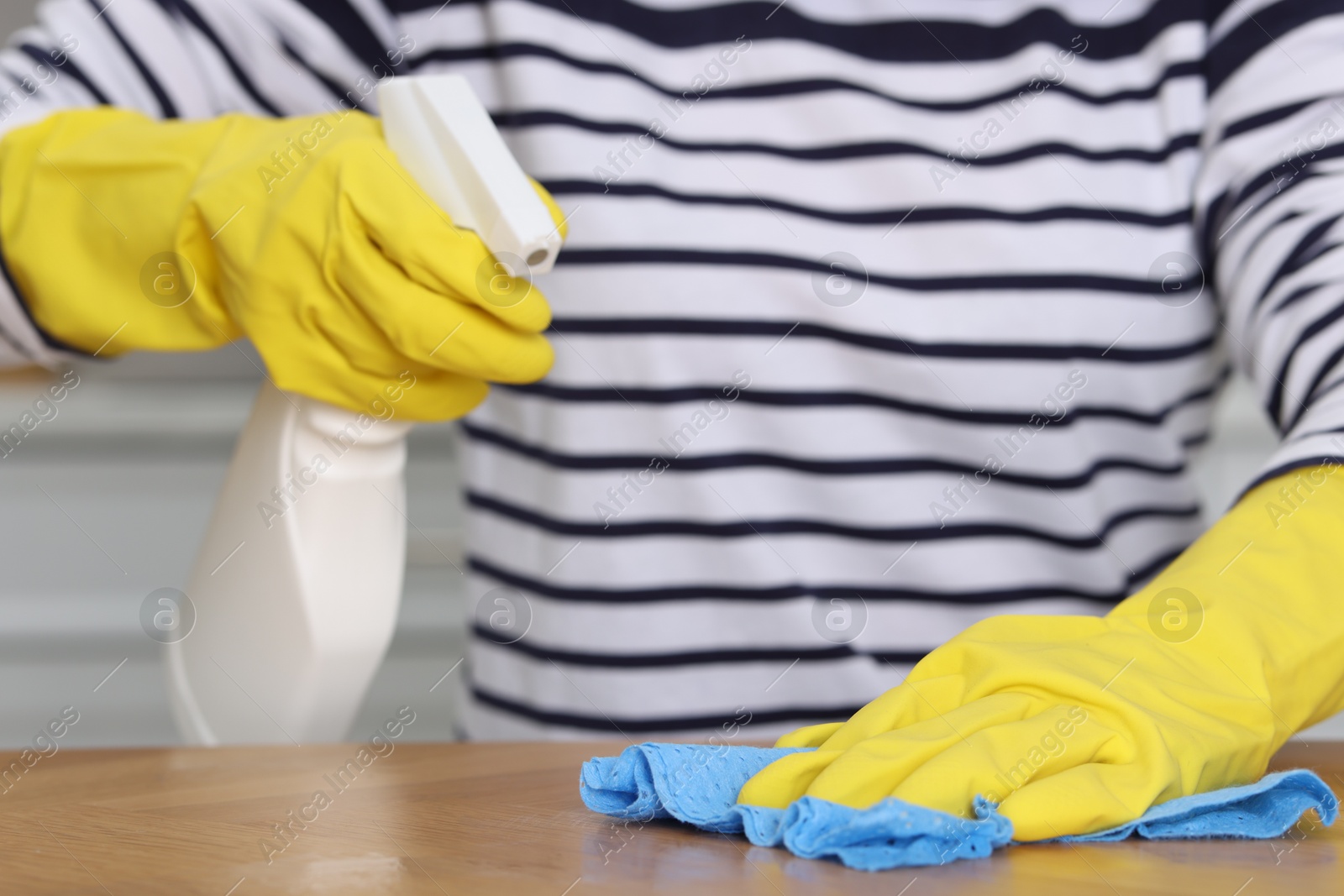 Photo of Woman using cleaning product while wiping wooden table with rag indoors, closeup