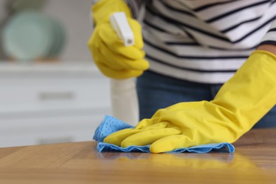 Photo of Woman using cleaning product while wiping wooden table with rag indoors, closeup