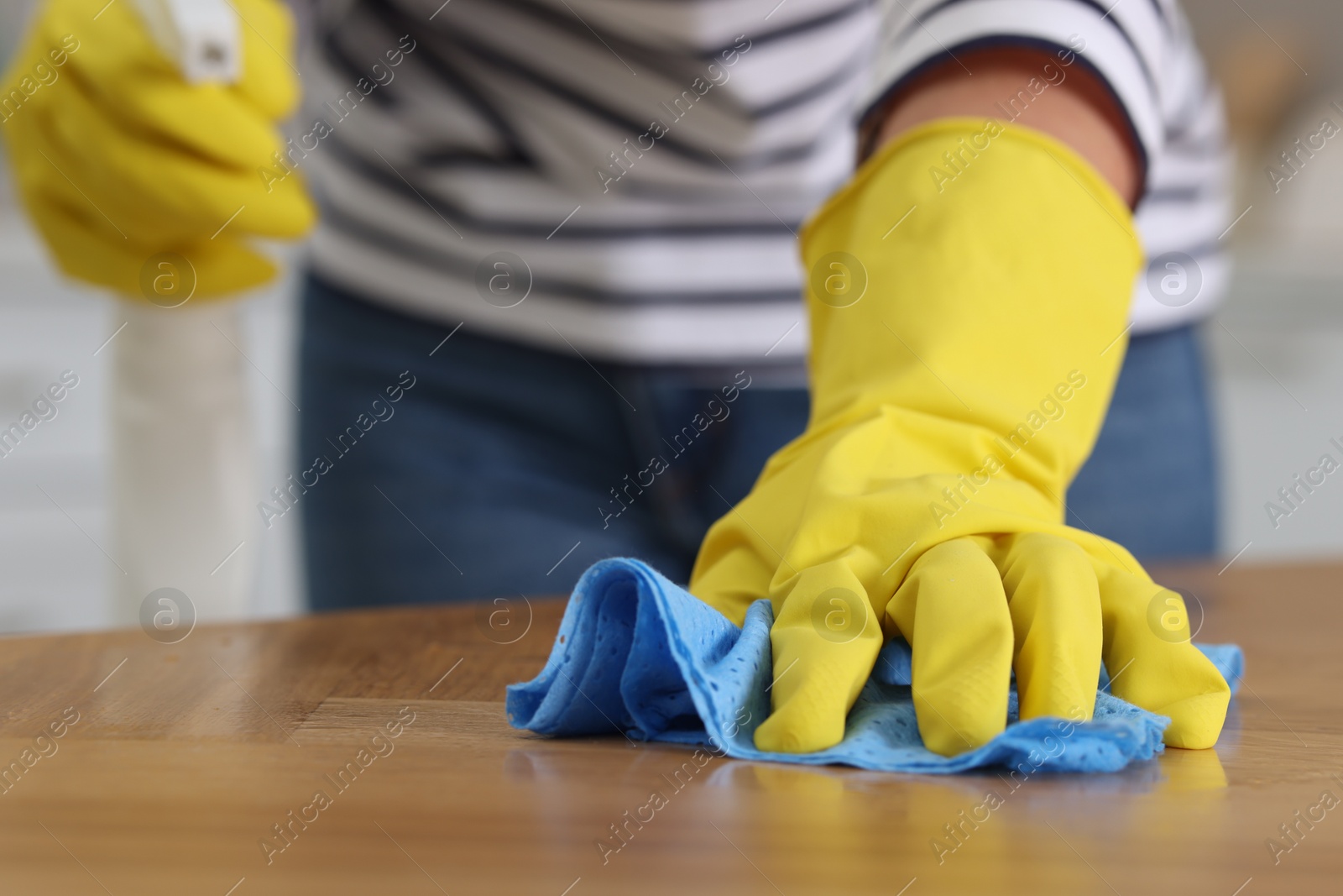 Photo of Woman using cleaning product while wiping wooden table with rag indoors, closeup