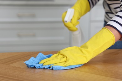 Photo of Woman using cleaning product while wiping wooden table with rag indoors, closeup. Space for text