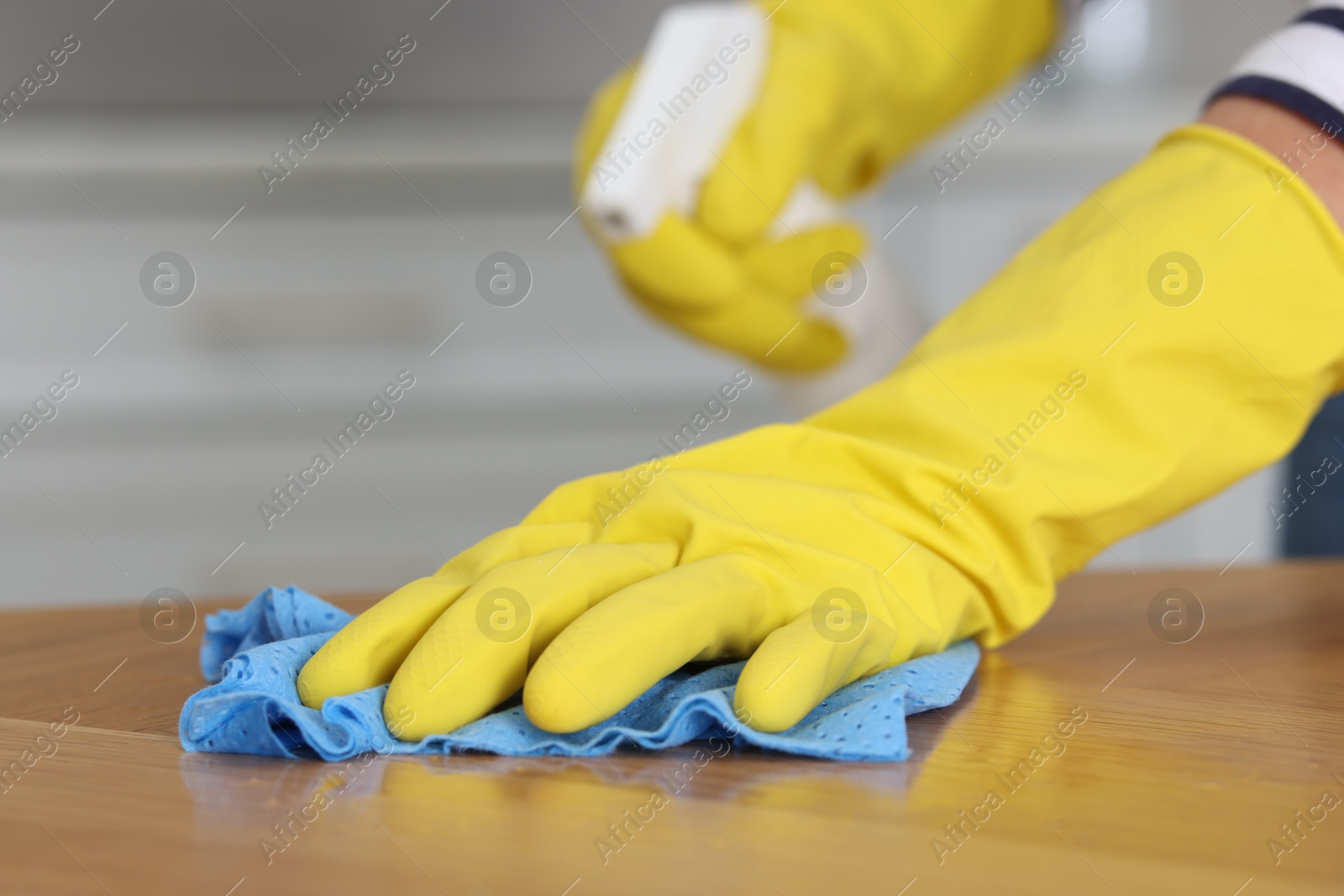 Photo of Woman using cleaning product while wiping wooden table with rag indoors, closeup