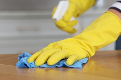 Photo of Woman using cleaning product while wiping wooden table with rag indoors, closeup