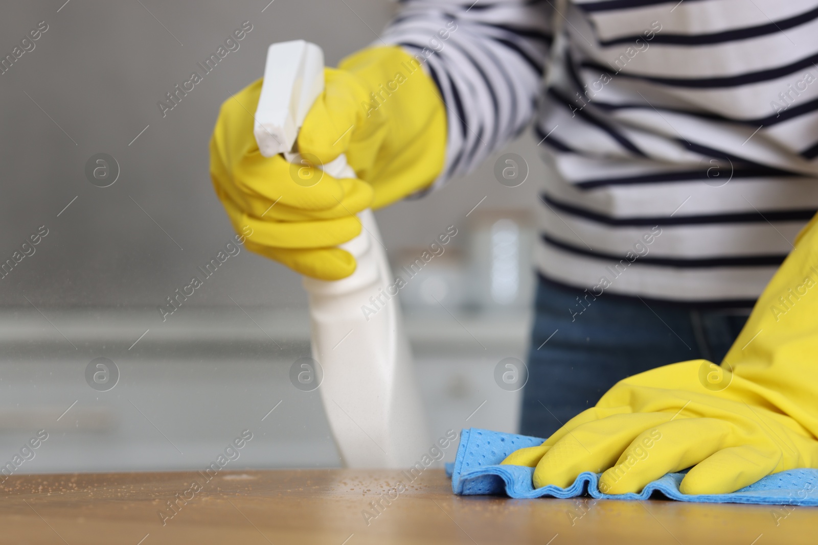 Photo of Woman using cleaning product while wiping table with rag indoors, closeup